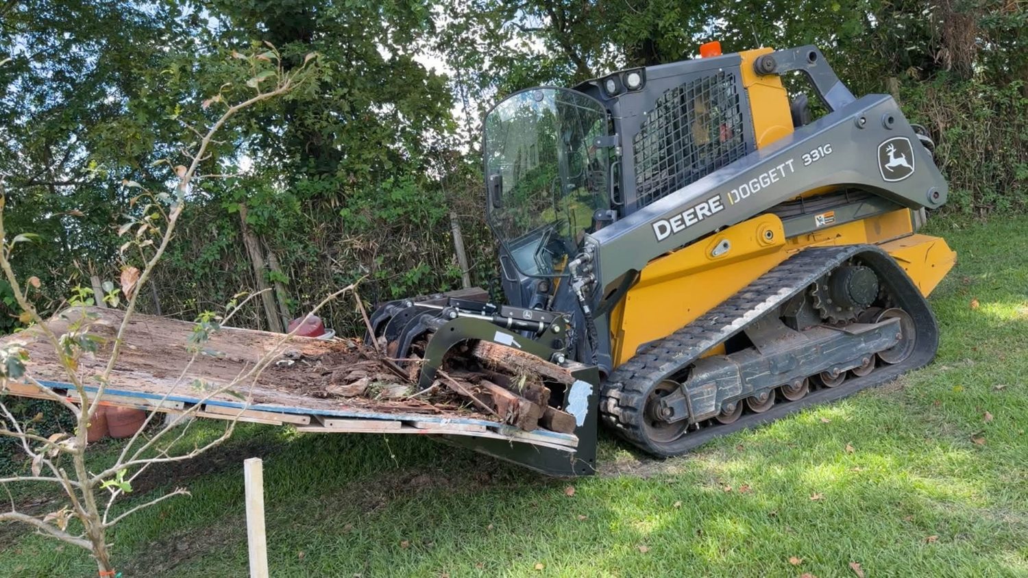 John Deere skid steer moving a large log using grapple attachment
